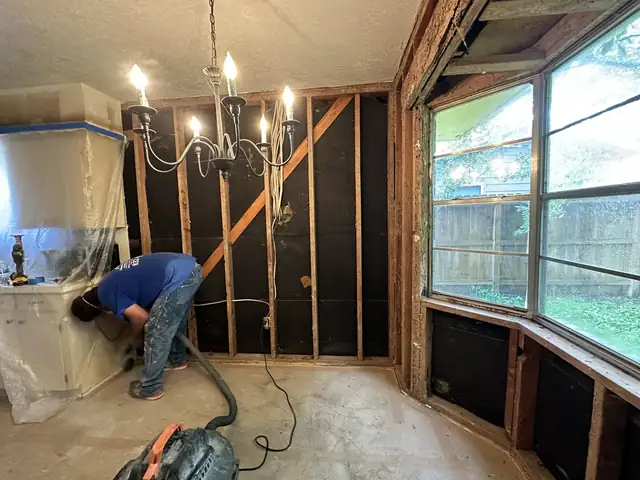 M&J crew member clearing a dining room stripped to the studs, with plastic sheeting protecting the next room