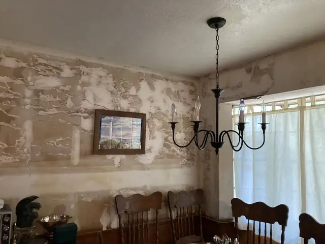 Dining room with stained, patched walls before repair, chandelier and wooden dining chairs